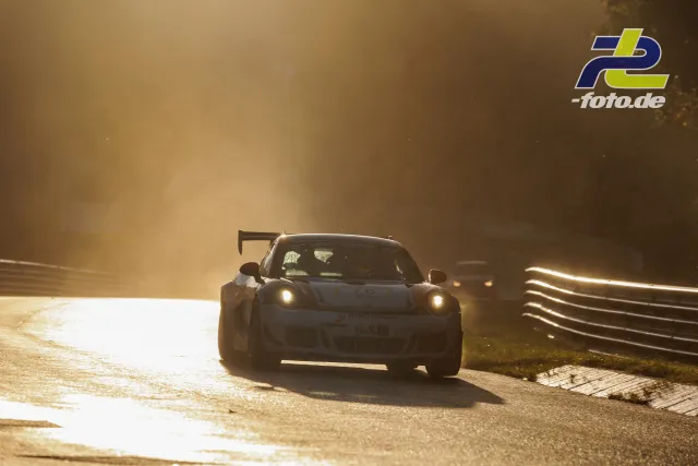 Porsche GT3-Rennwagen im Gegenlicht bei Sonnenuntergang auf dem Nürburgring, weiteres Fahrzeug folgt im Hintergrund.