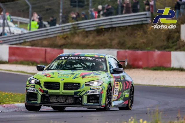 BMW M2 #877 mit giftgrüner Lackierung in einer Kurve auf dem Nürburgring bei der NLS Sportwarte-Trophy, Zuschauer im Hintergrund.