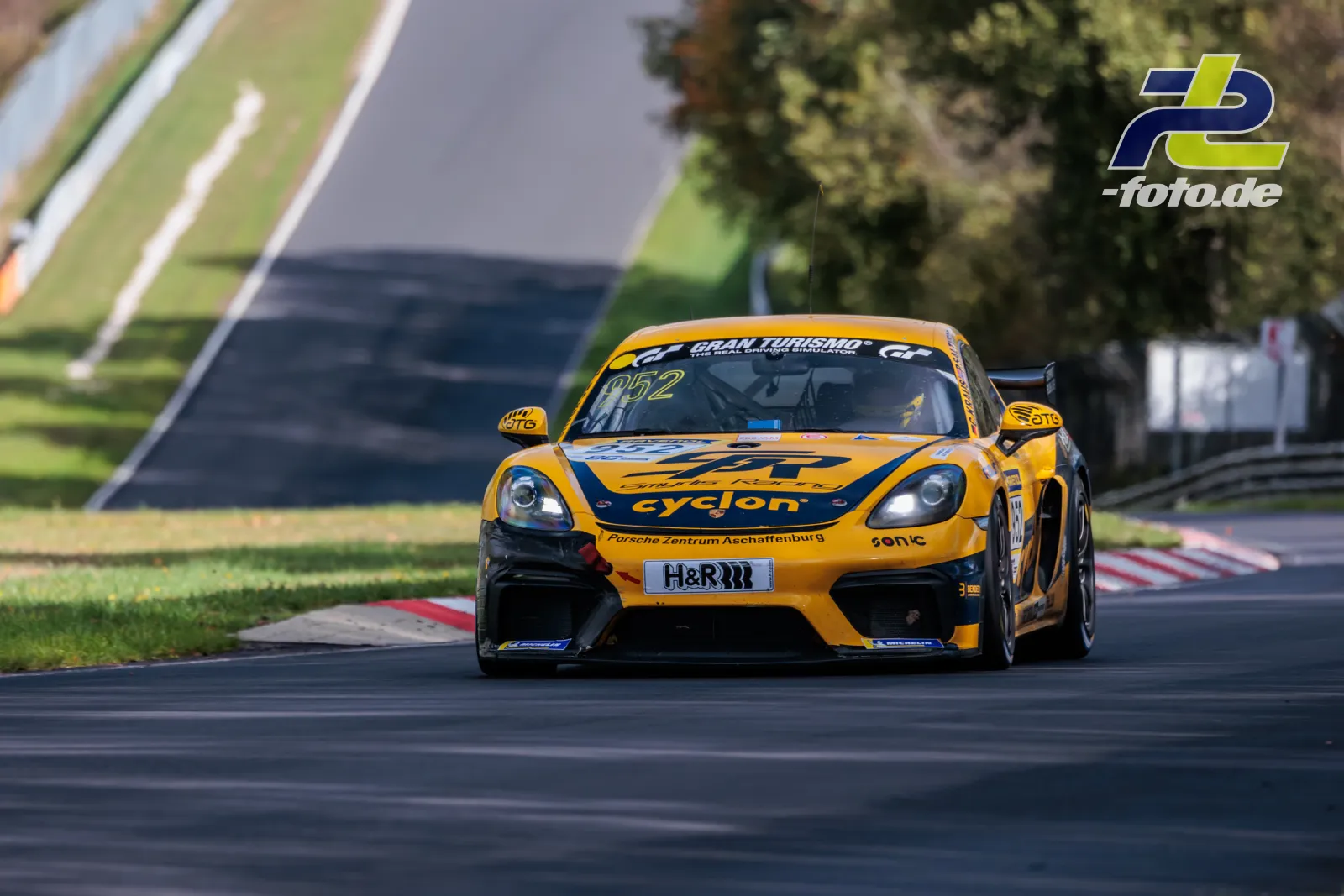 Porsche Cayman GT4 in gelb-schwarzer cyqlon-Lackierung in Kurvenausfahrt auf der Nürburgring-Nordschleife beim NLS-Rennen