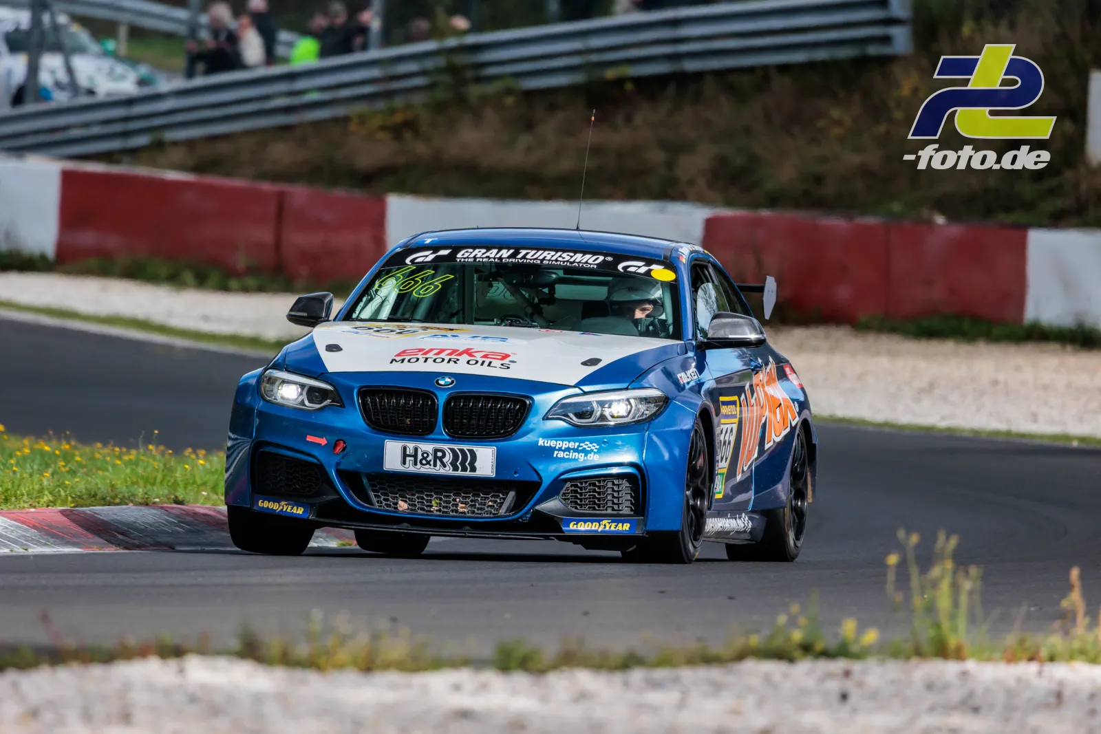 BMW M240i in blau-weißer Lackierung von Kuepper Racing auf der Nürburgring-Nordschleife während des Rennens, Zuschauer im Hintergrund.