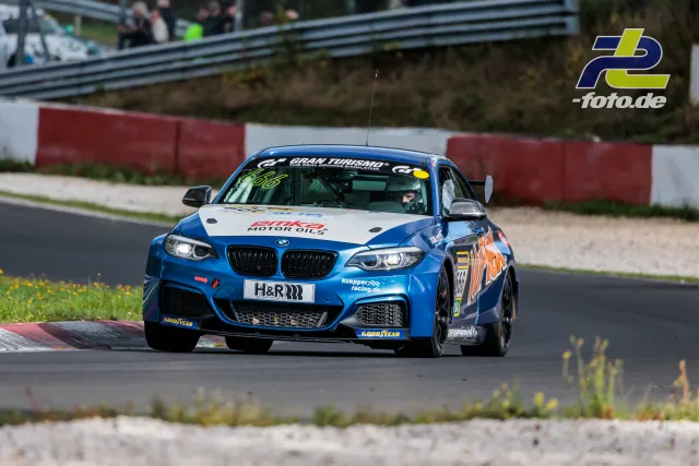 BMW M240i in blau-weißer Lackierung von Kuepper Racing auf der Nürburgring-Nordschleife während des Rennens, Zuschauer im Hintergrund.