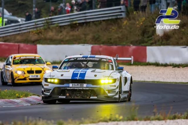 Weißer Ford Mustang GT3 mit blauem Streifen vom HAUPT Racing Team vor gelbem BMW auf dem Nürburgring während des NLS-Rennens.