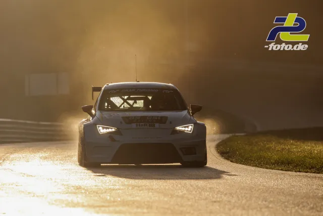 TCR-Tourenwagen in Frontalansicht bei Gegenlicht auf nasser Strecke mit eingeschalteten Scheinwerfern während des Qualifyings am Nürburgring.
