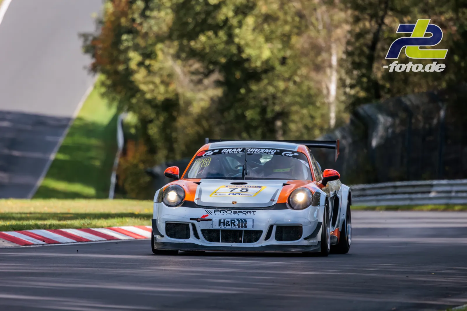 Porsche Cayman Pro4 von PROsport racing in weiß-oranger Lackierung während des NLS-Rennens auf dem Nürburgring bei Tageslicht.