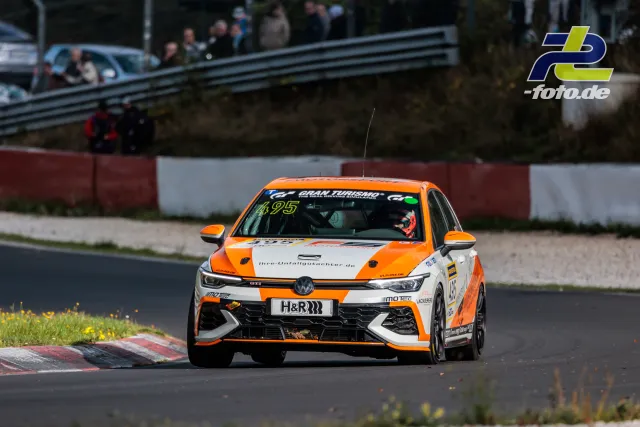 VW Golf GTI mit orange-weißer Lackierung in Kurve auf der Nordschleife, Zuschauer am Streckenrand, Randsteine im Vordergrund