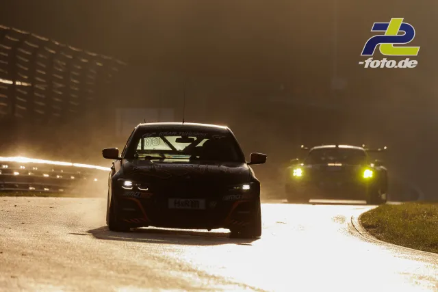 Zwei Rennwagen im Gegenlicht auf der Nürburgring-Nordschleife während des Qualifyings. Dramatische Lichtstimmung mit Staub oder Sprühnebel.