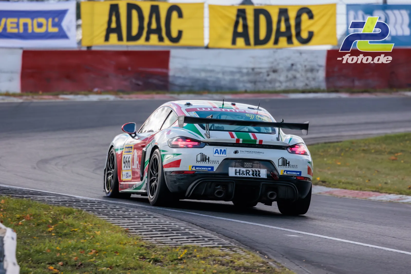 Porsche Cayman GT4 mit Startnummer 966 in Heckansicht auf der Nordschleife, ADAC-Banden im Hintergrund.