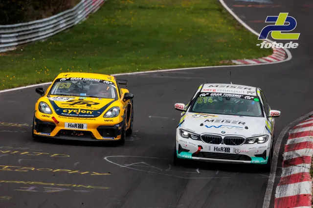 Ein gelber Porsche und ein weißer BMW fahren durch eine Kurve auf der Nürburgring-Nordschleife während eines NLS-Rennens.