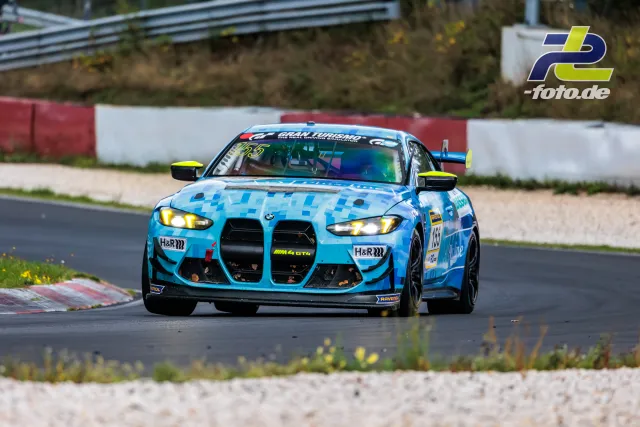 BMW M4 GT4 #155 in hellblauem Pixeldesign mit neongelben Spiegeln auf der Nürburgring-Nordschleife beim NLS-Rennen.