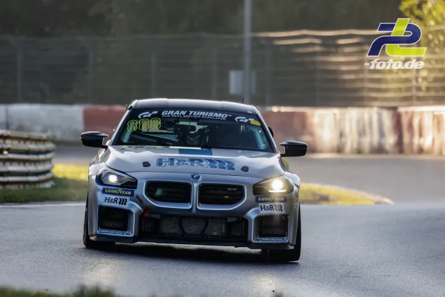 BMW Rennwagen 888 mit weißer Lackierung fährt frontal auf der Strecke, Frontscheinwerfer eingeschaltet